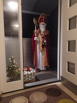 Foto vom Nikolaus vor einer geöffneten Tür eines Hauses